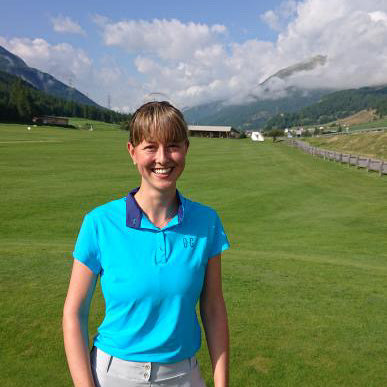 Image of woman wearing Ocean Meets Green Moana golf polo in light blue and Tide skirt in grey, standing on a putting green