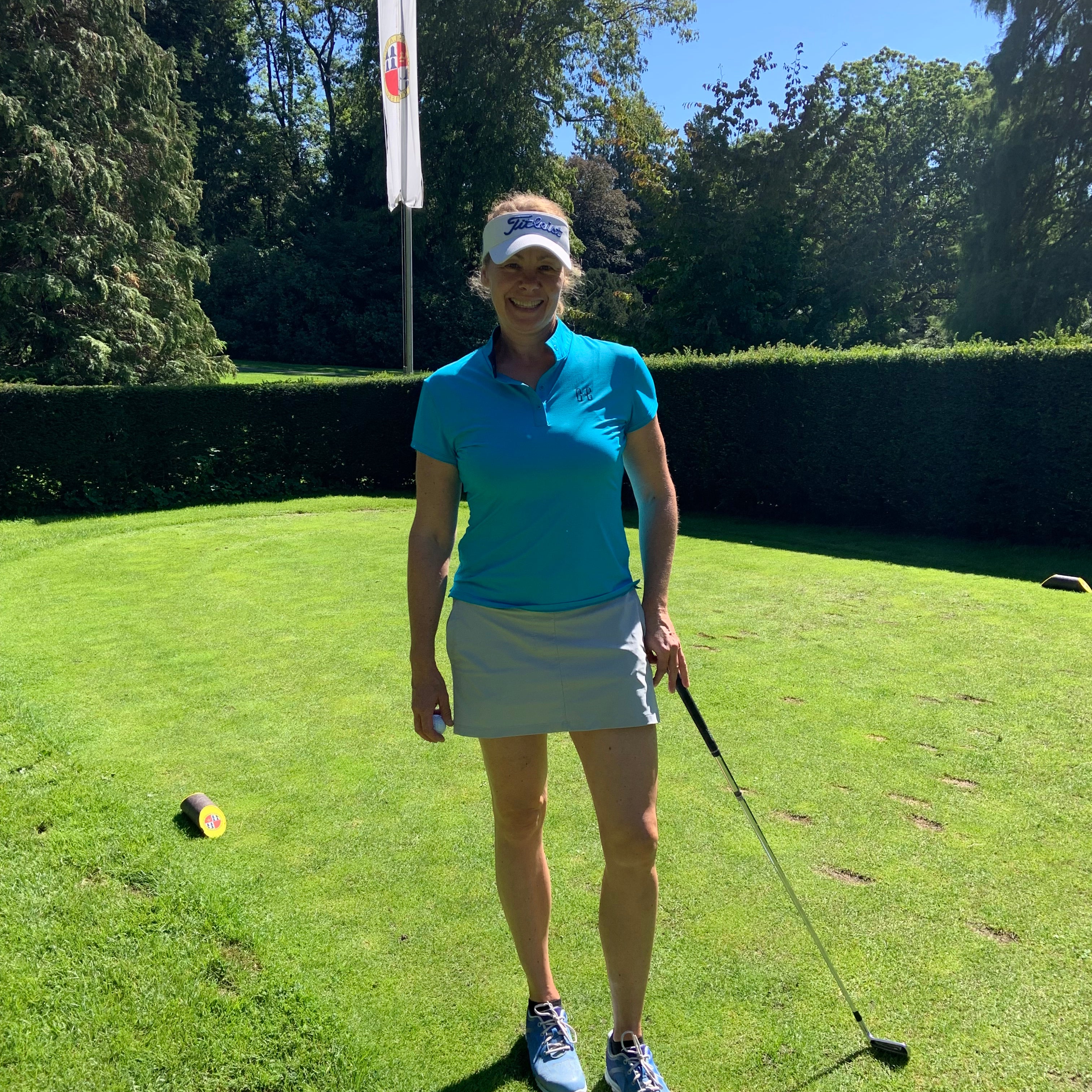 Image of woman wearing Ocean Meets Green Moana golf polo in light blue and Tide skirt in grey, standing on a teebox