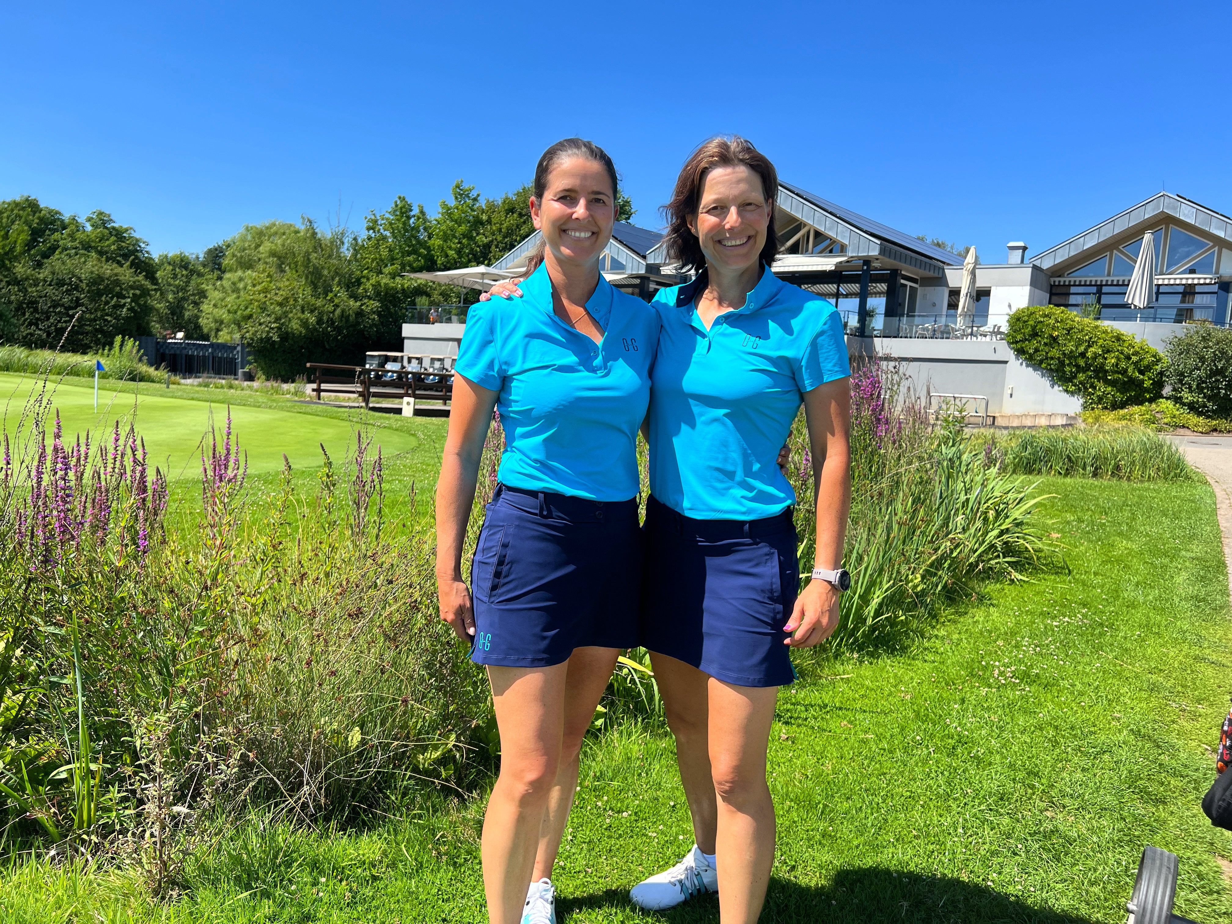 Image of two women wearing Ocean Meets Green outfits: Moana golf polo in light blue and Tide skirt in navy