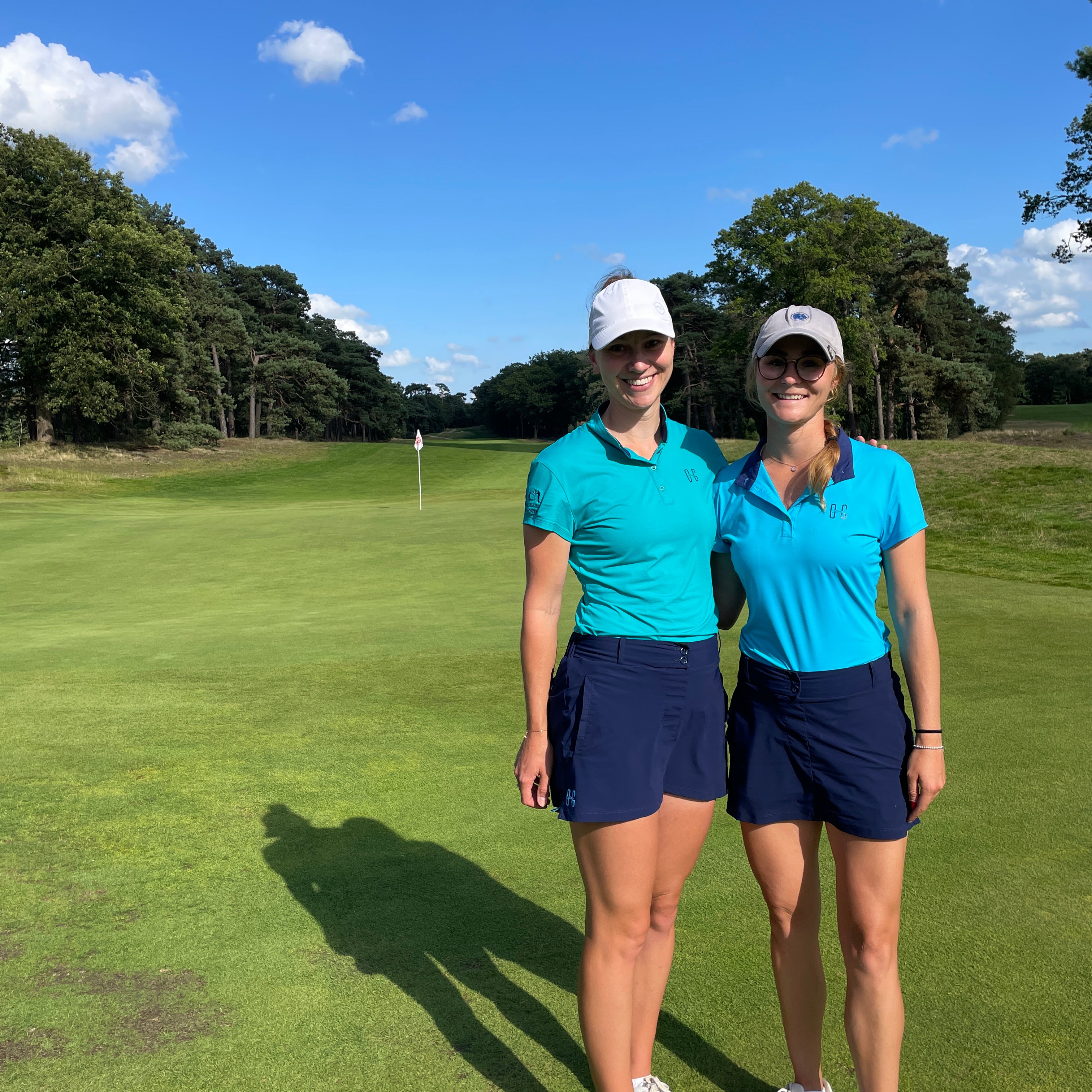 Image of two women wearing Ocean Meets Green outfits: Moana golf polo in light blue and Tide skirt in navy + Moana golf polo in green and Tide skirt in navy