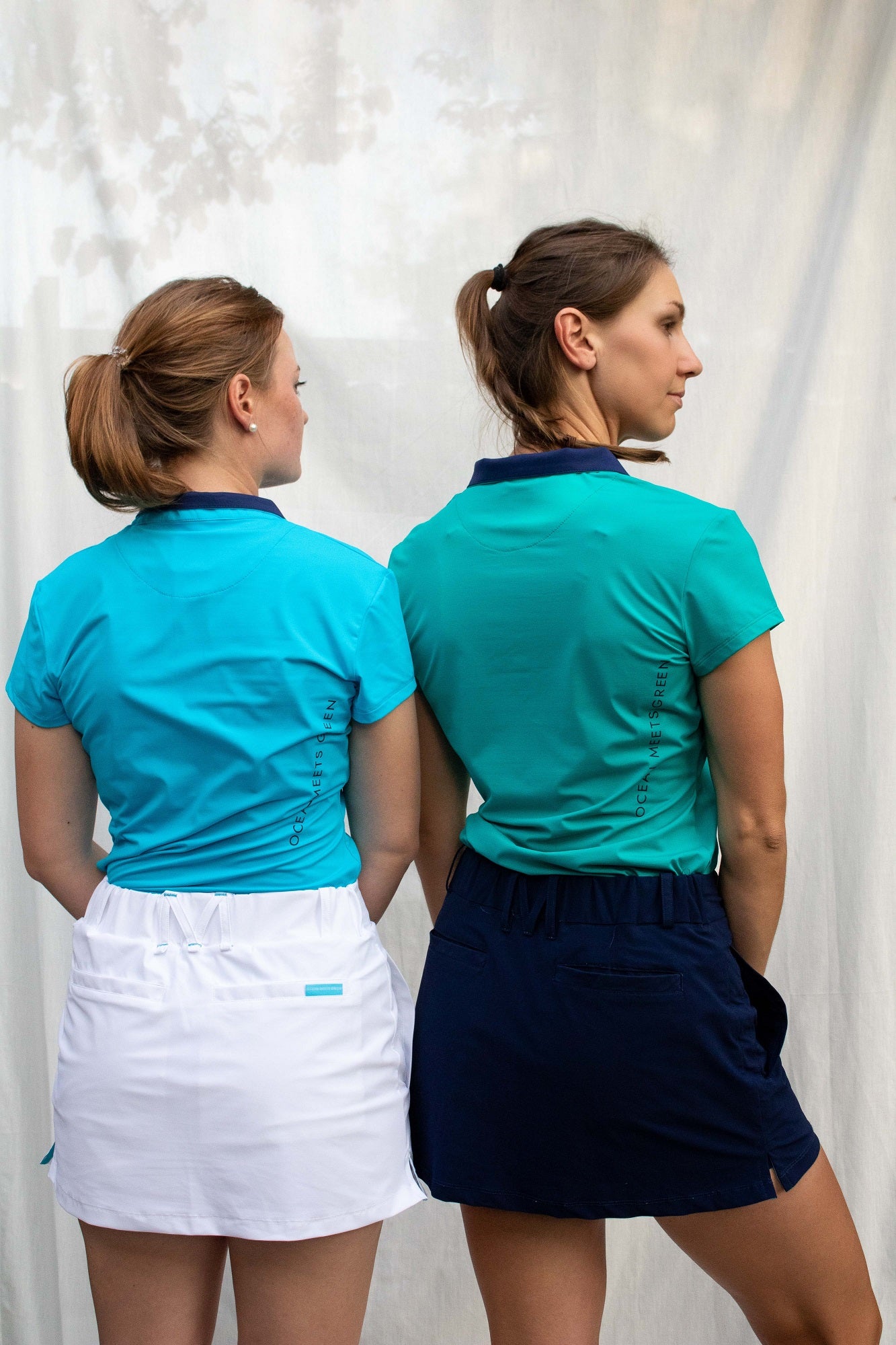 Image of two women wearing Ocean Meets Green outfits: Moana golf polo in light blue and Tide skirt in white + Moana golf polo in green and Tide skirt in navy