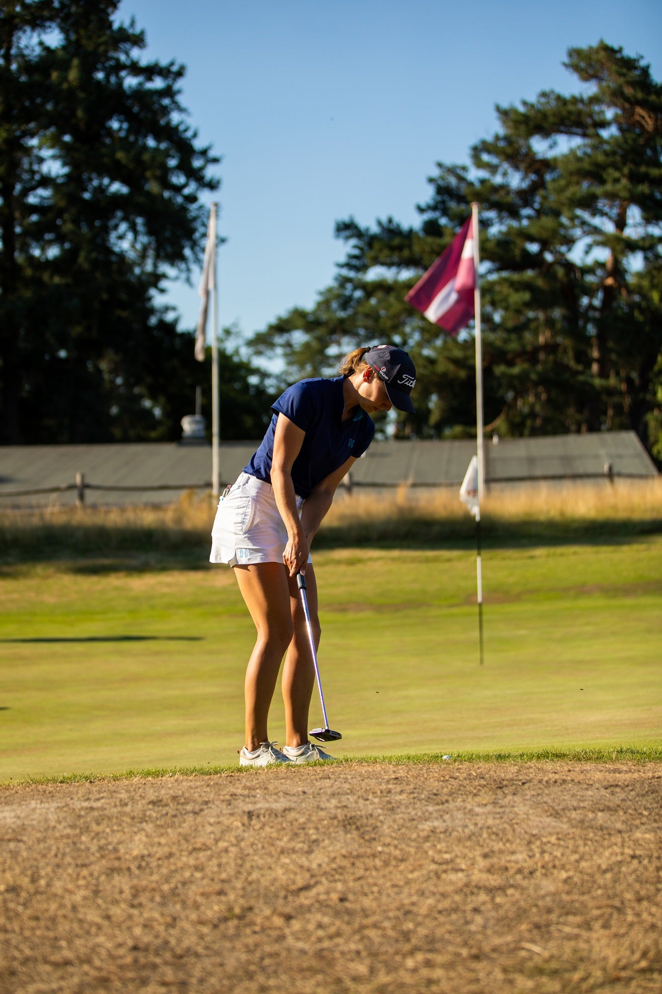 Image of woman wearing Ocean Meets Green Moana golf polo in navy and Tide skirt in white, putting