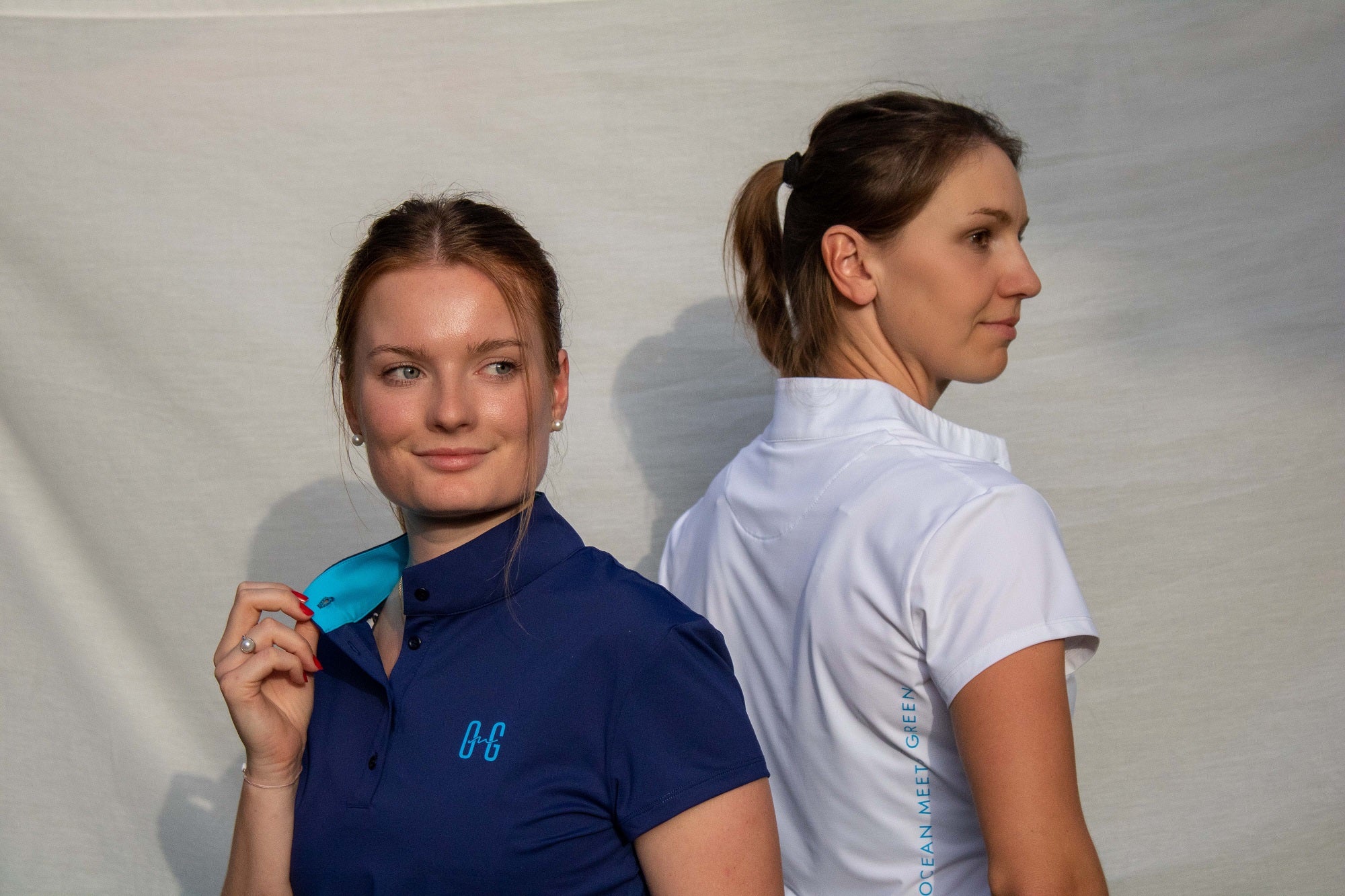 Image of two women wearing Ocean Meets Green Moana golf polo in navy + white