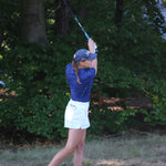 Image of woman wearing the Ocean Meets Green TIDE skirt in white and the MOANA poloshirt in navy