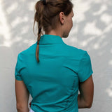 Full body image of Ocean Meets Green women's golf polo Moana in green worn by a woman, showing the side logo