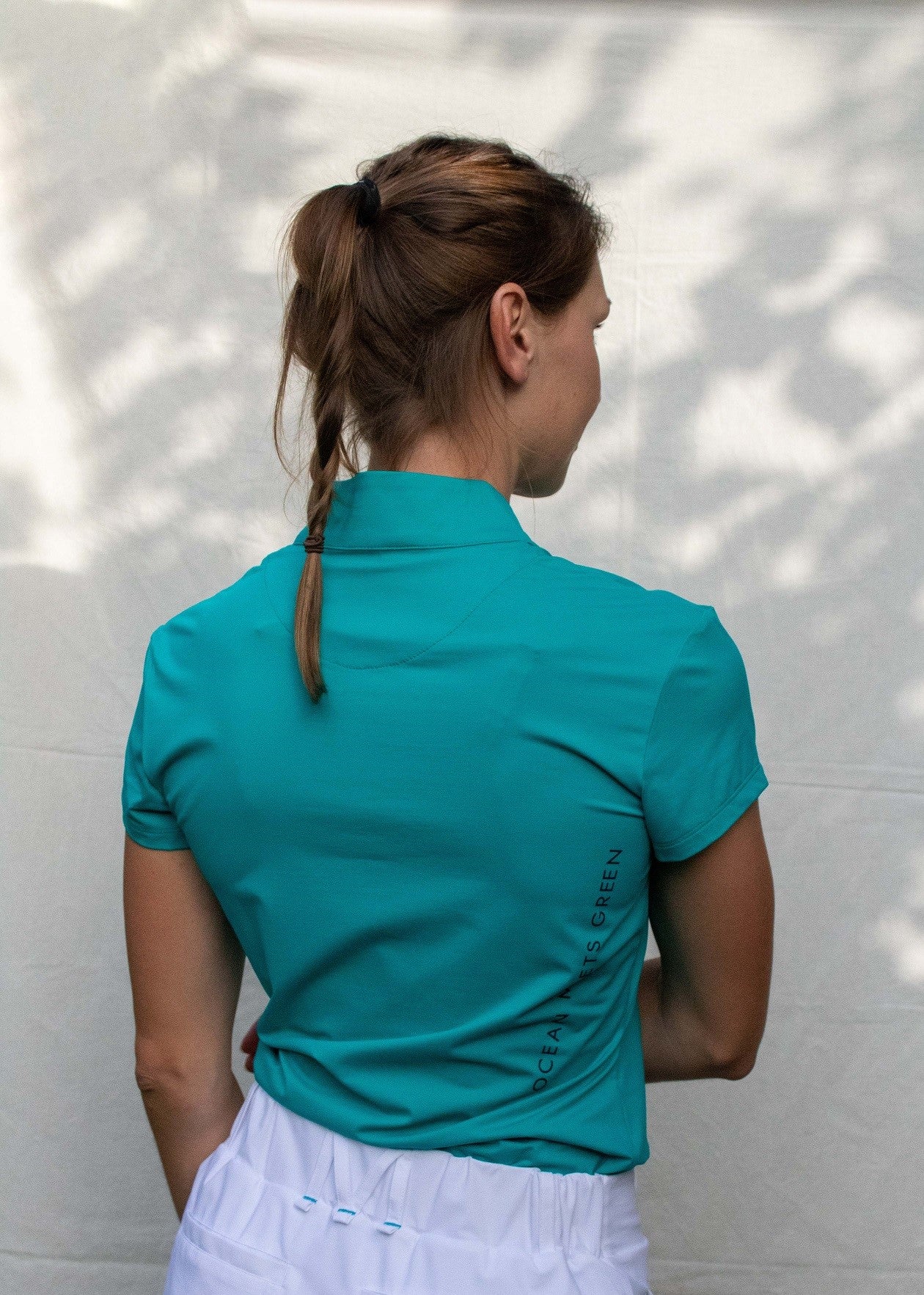 Full body image of Ocean Meets Green women's golf polo Moana in green worn by a woman, showing the side logo