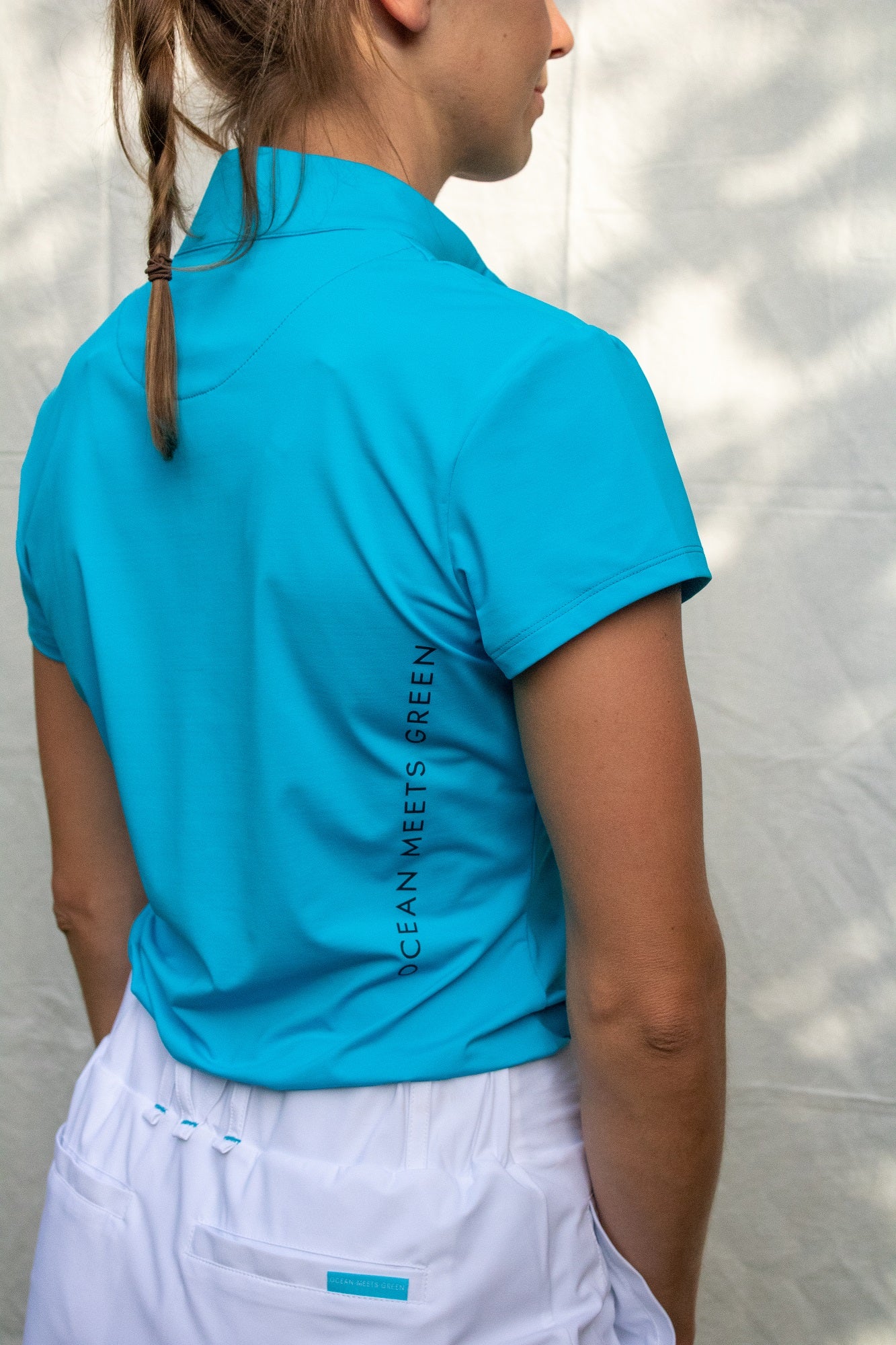 Full body image of Ocean Meets Green women's golf polo Moana in light blue worn by a woman, showing the side logo