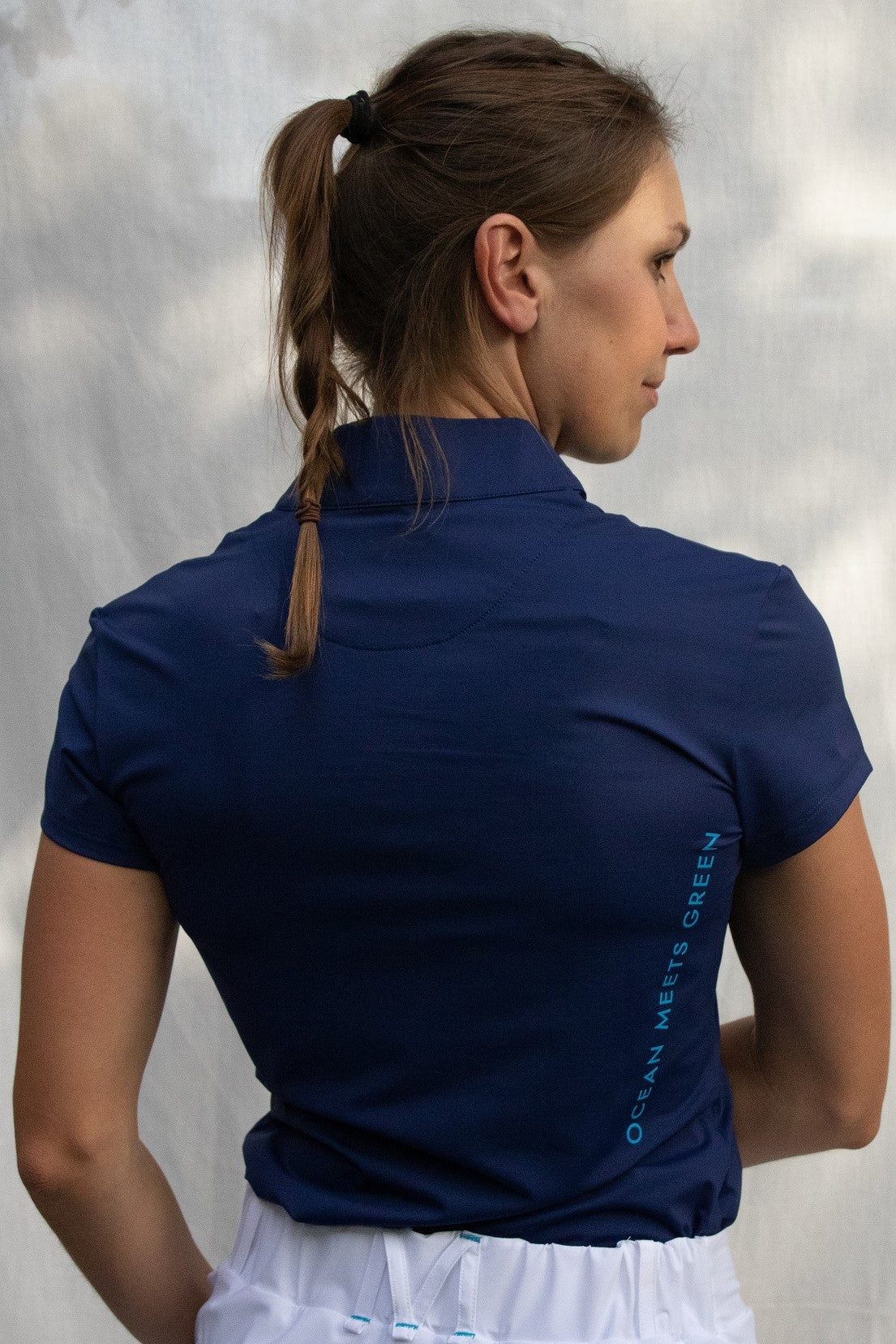 Full body image of Ocean Meets Green women's golf polo Moana in navy worn by a woman, showing the side logo